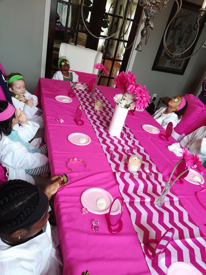 Pink spa party table with girls in robes enjoying cucumber facials and pampering